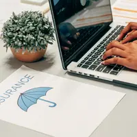 A laptop and an insurance document with an umbrella icon on a desk
