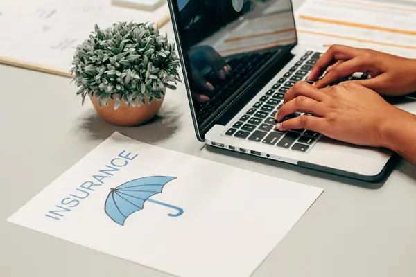 A laptop and an insurance document with an umbrella icon on a desk